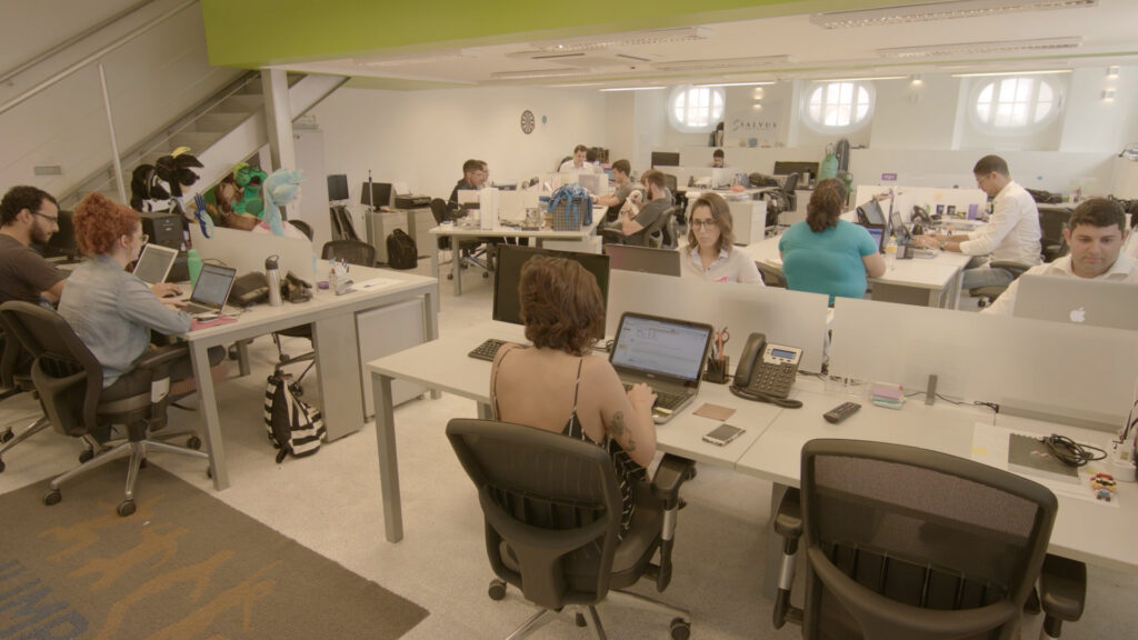 Pessoas trabalhando em um escritório moderno com computadores e mesas, representando um ambiente de colaboração em uma micro ou pequena empresa.