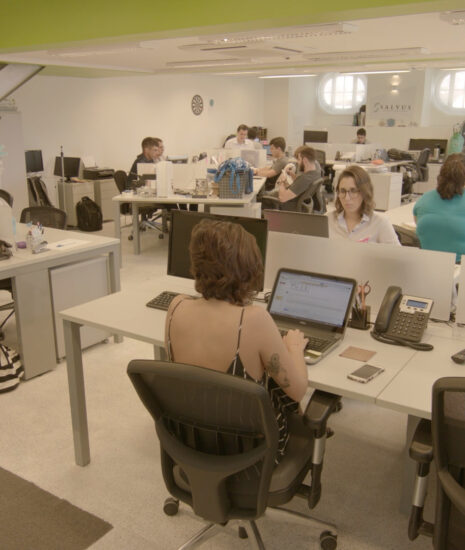Pessoas trabalhando em um escritório moderno com computadores e mesas, representando um ambiente de colaboração em uma micro ou pequena empresa.