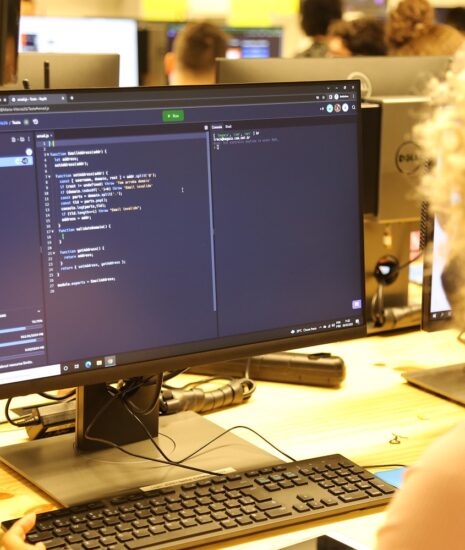 Aluna com cabelos cacheados claros concentrada programando em um computador. A tela exibe código, indicando a formação em desenvolvimento de software.
